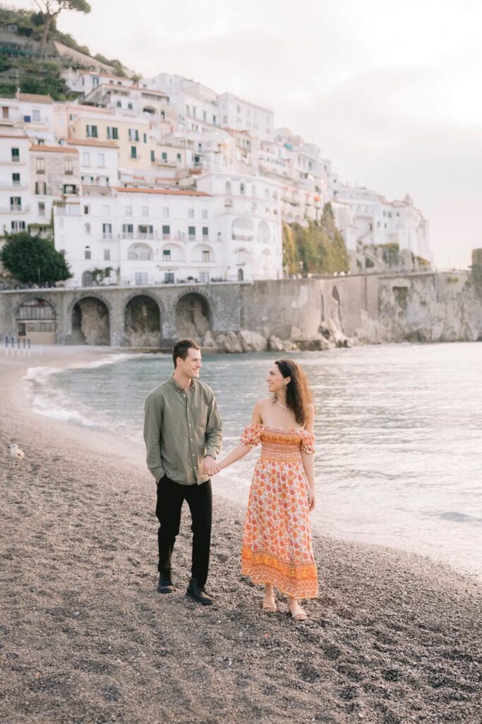 A couple walking on the beach in Amalfi Village on the Amalfi Coast, which is one of the best places to visit in Italy, on a couples photoshoot with Flytographer.