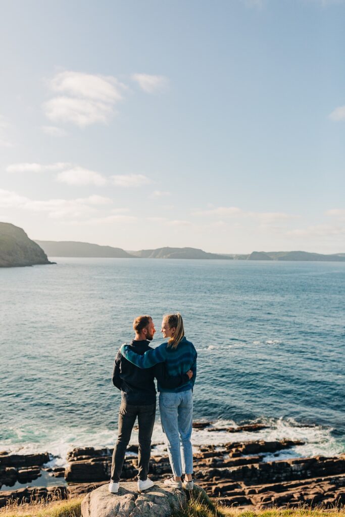 Couple looking at the view with a lighthouse behind them in St. John's Newfoundland on vacation in the summer captured by Flytographer