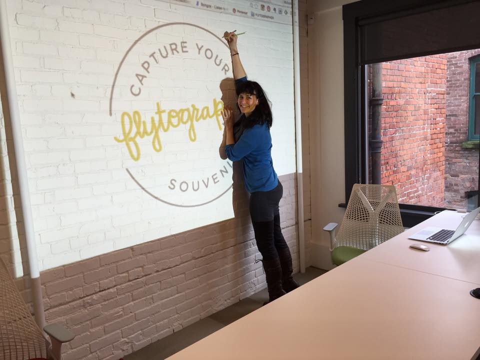 Michelle tracing our logo on the white brick wall, right before painting it on. We heart our office.