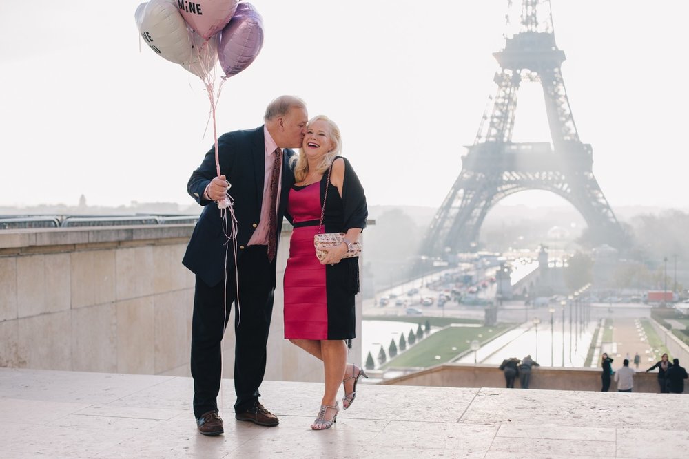 Man kissing his partner's cheek while holding balloons with the Eiffel Tower in the background in Paris, France