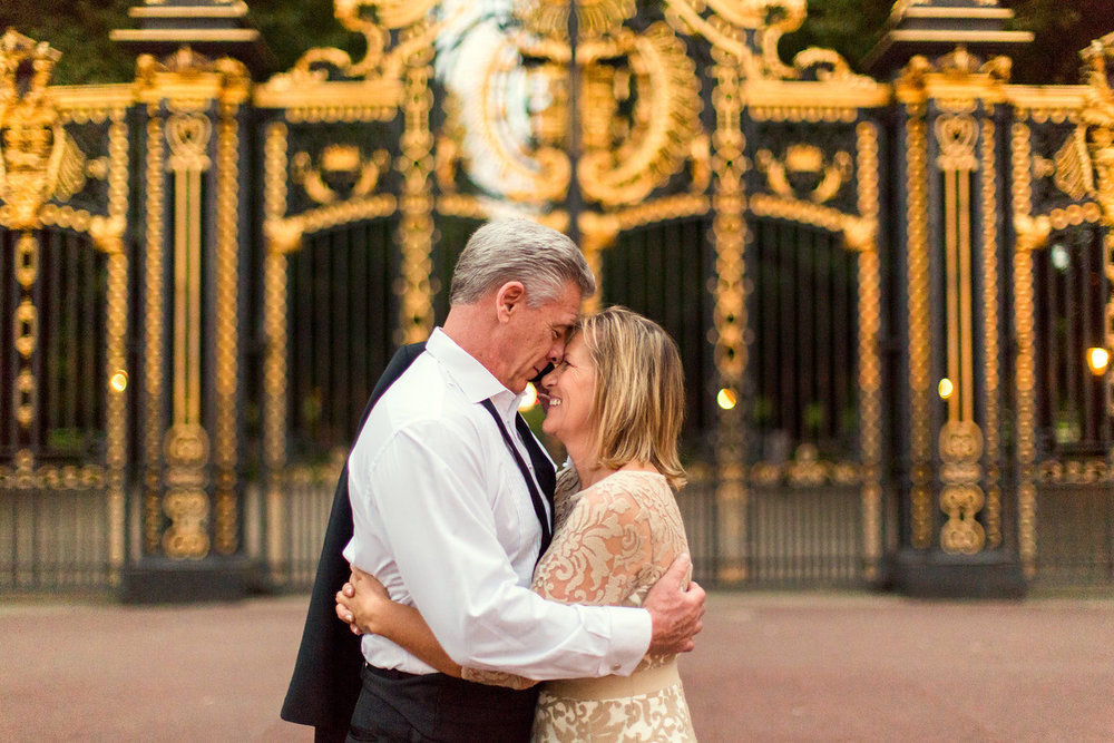 Mature couple hugging each other in front of the gates at Buckingham Palace in London, UK